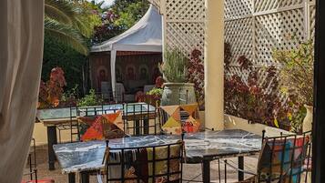 Un patio al aire libre con mesas y sillas, una cerca decorativa y vistas a un edificio con arcos.