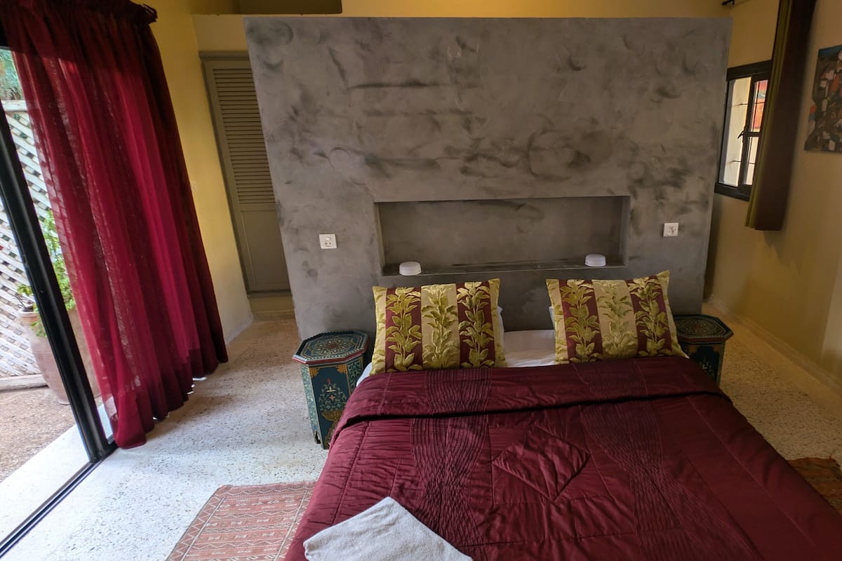A bedroom with a bed, two pillows, a nightstand, a window, and a door.