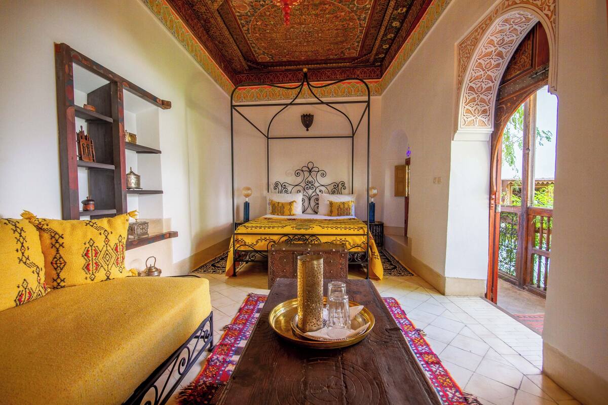 A traditional room with a bed, a sofa, a table with a tray, and a decorative ceiling.