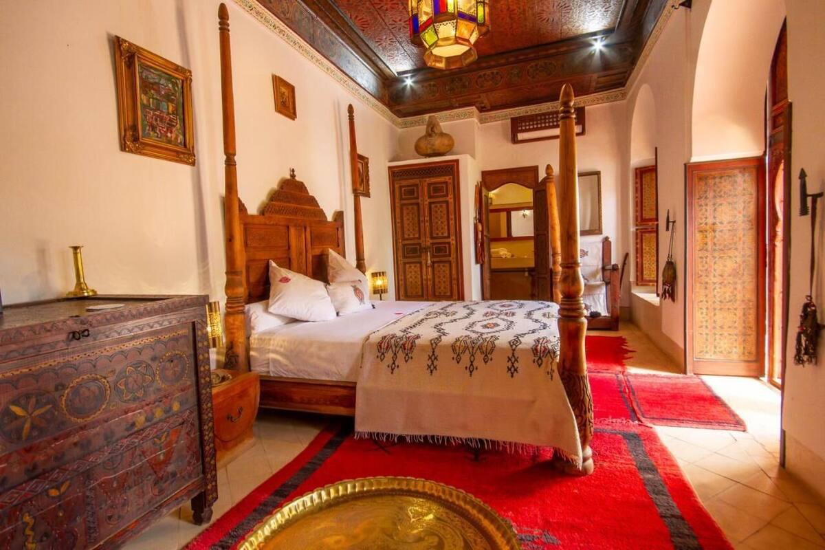 A traditional room with a four-poster bed, ornate wooden furniture, and a red carpet.