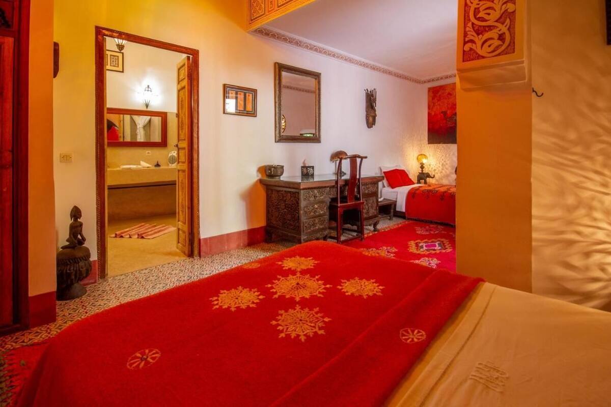 A room with a bed, a desk, a chair, and a mirror. There is a red carpet on the floor.