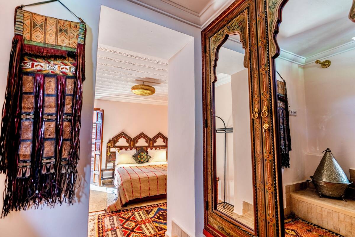 A room with a bed, a large ornate mirror, and a traditional Moroccan-style lamp.