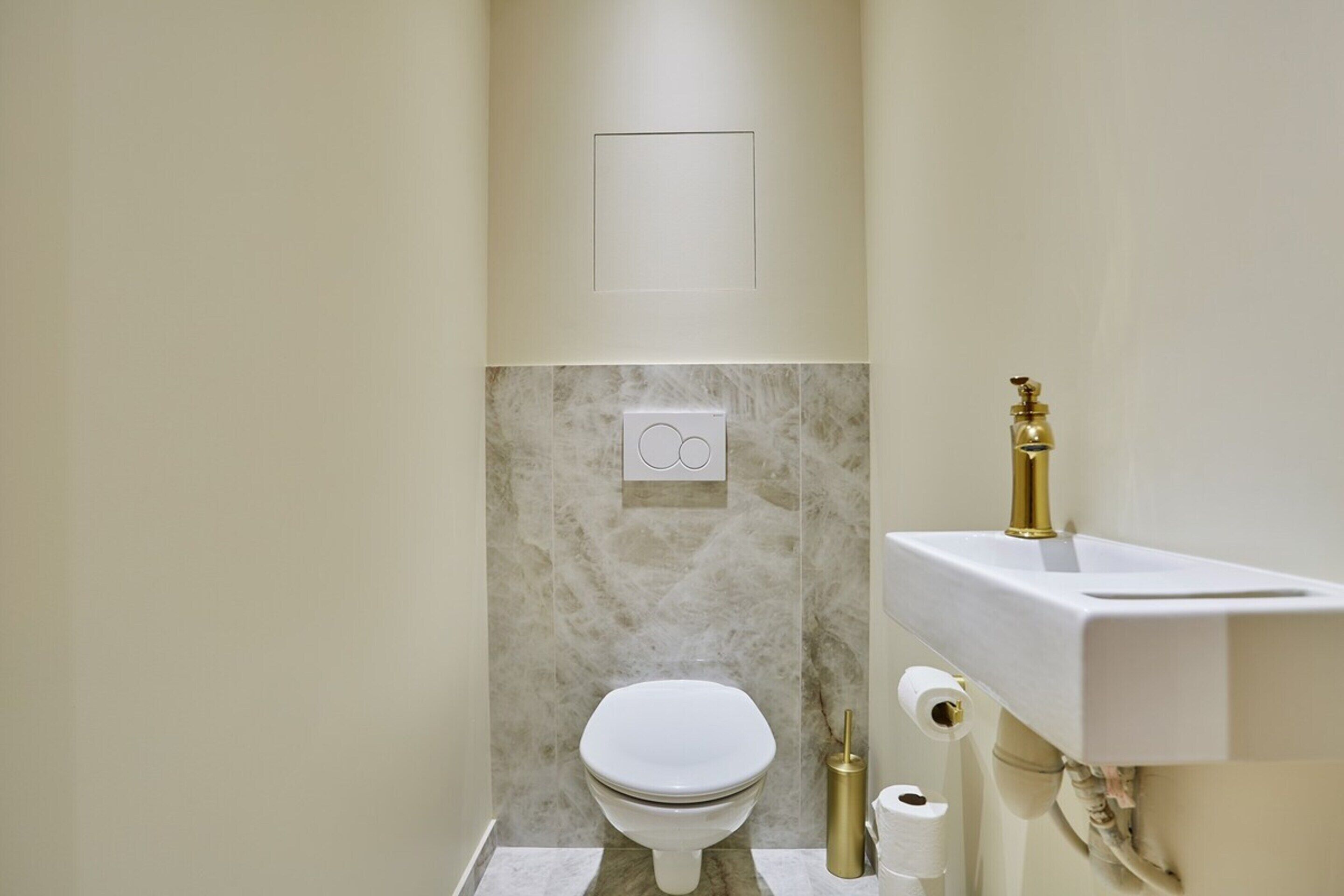 Ein modernes Badezimmer mit Toilette, Waschbecken und einer Wand aus Marmorfliesen.
