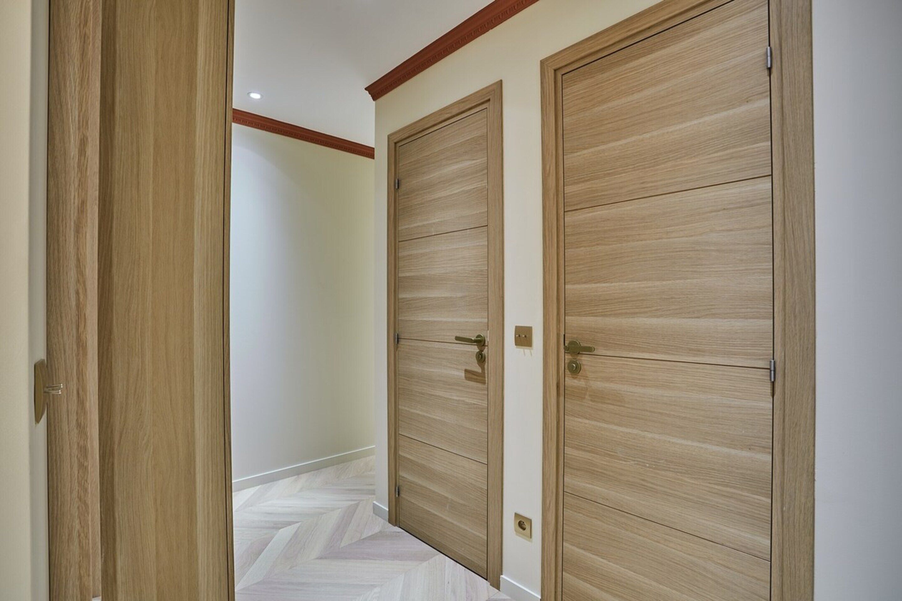 Un couloir avec deux portes en bois, un plancher en bois et un plafond doté d’un éclairage encastré.