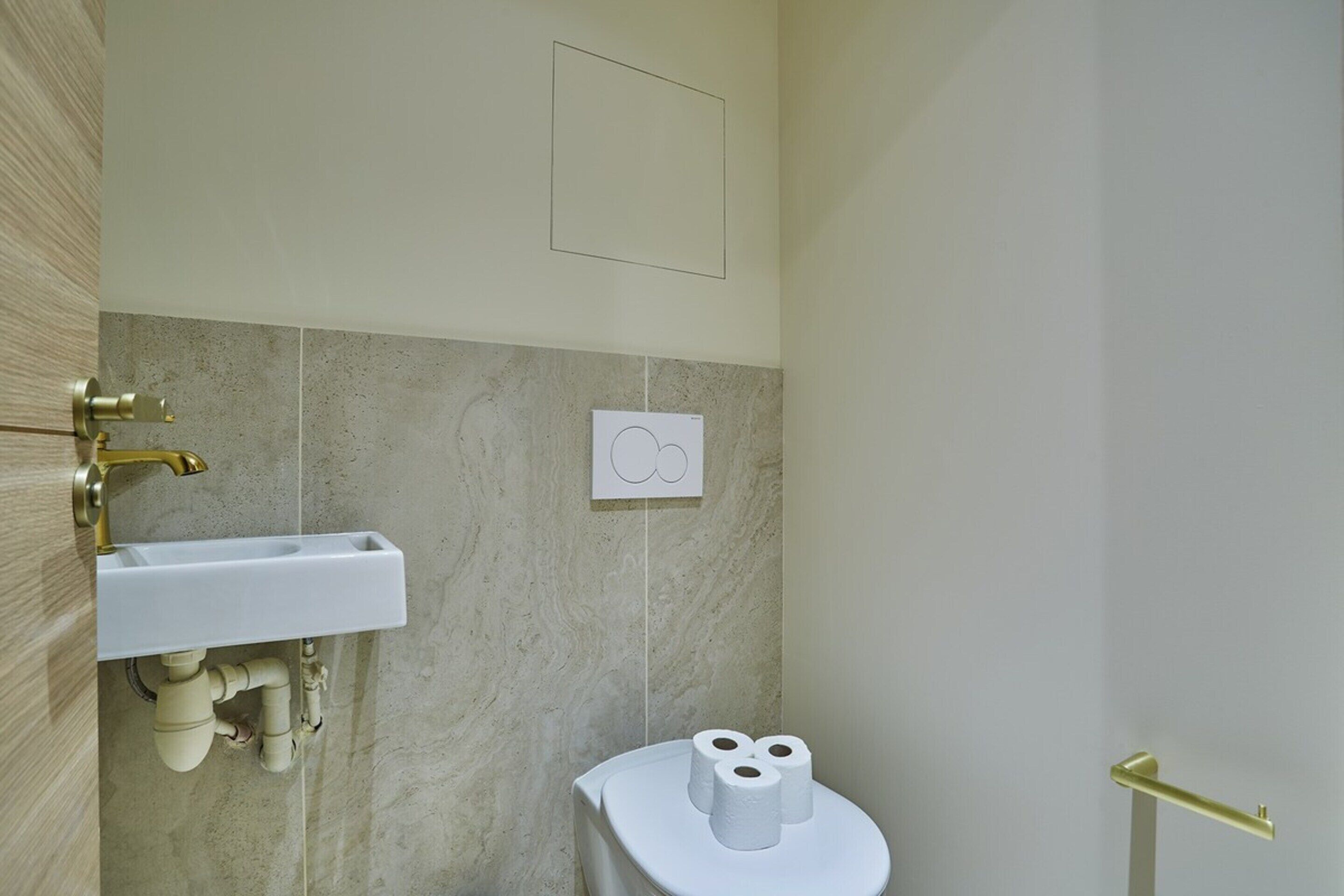 A bathroom with a white sink, marble walls, and a toilet with two rolls of toilet paper.