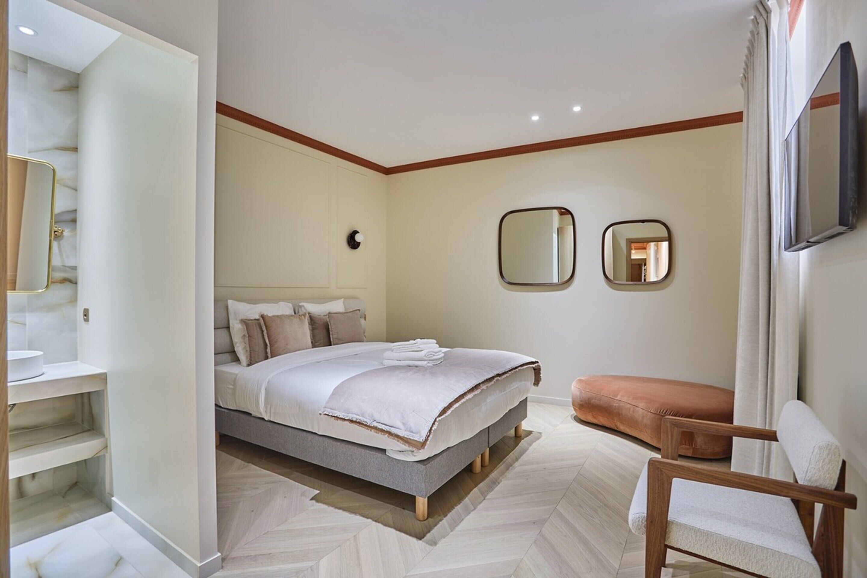 Een moderne slaapkamer met een bed, een houten stoel, een spiegel en een televisie.