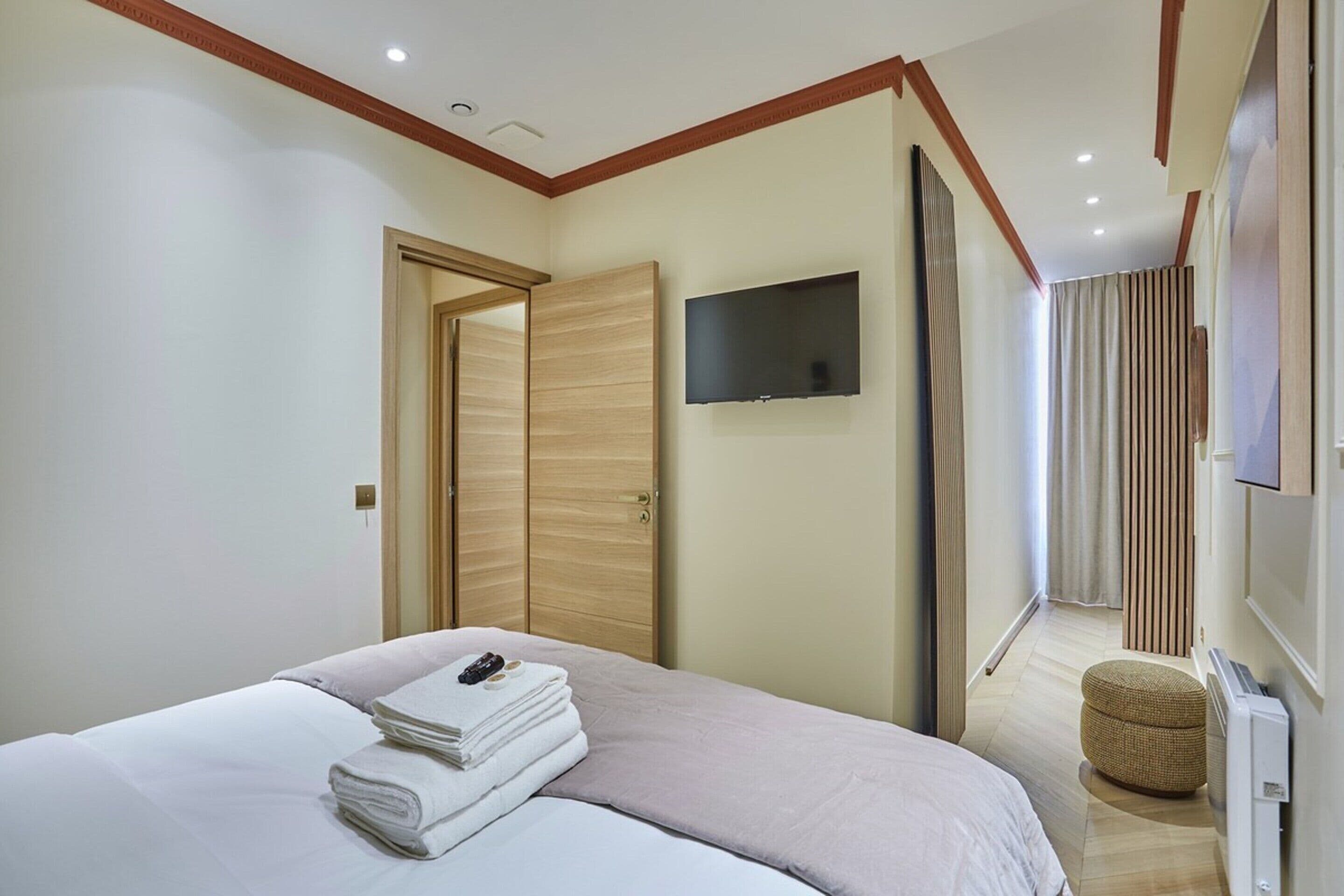 Una habitación de hotel moderna con una cama, un televisor de pantalla plana en la pared y un armario de madera.
