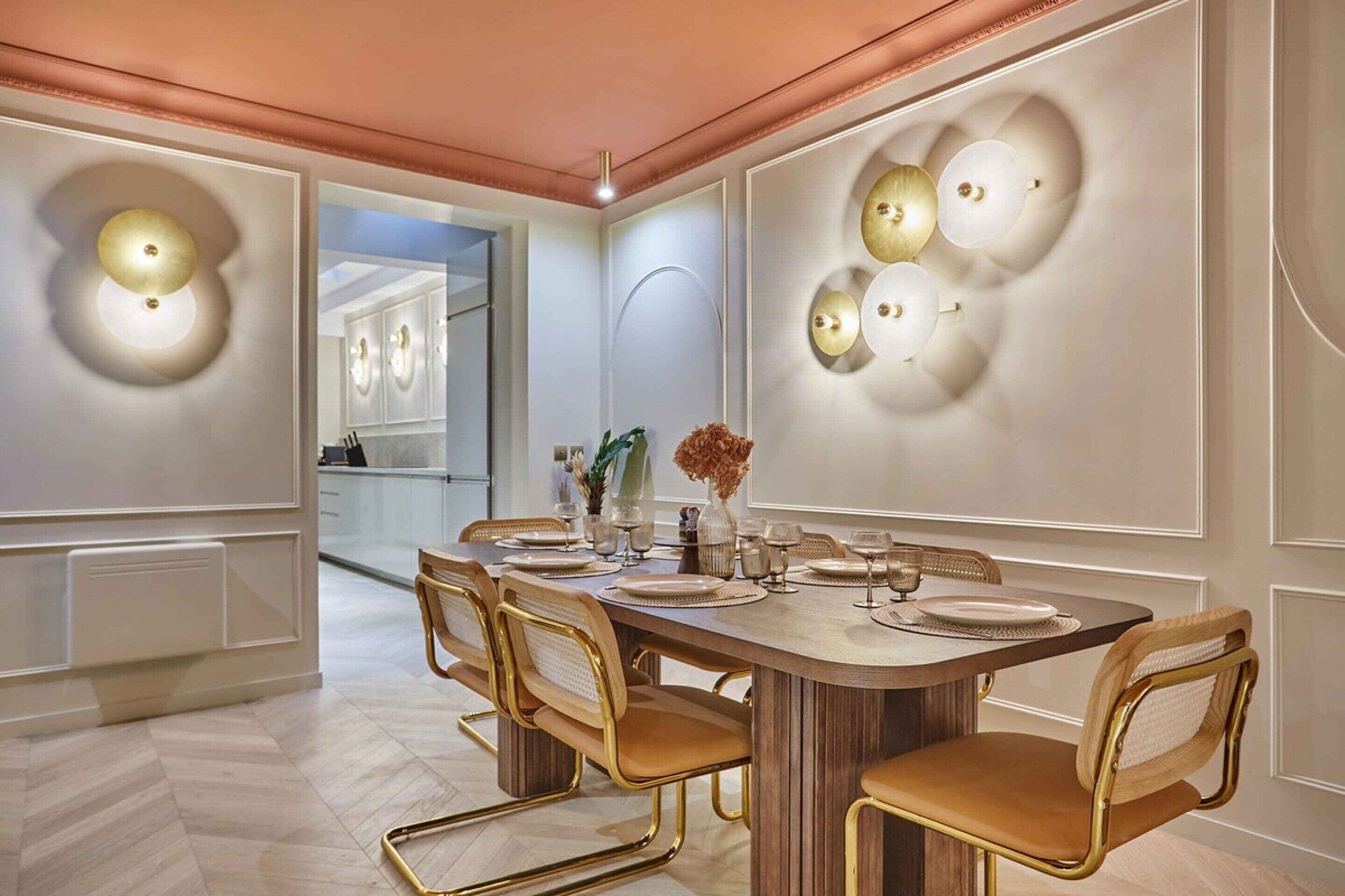 Un coin repas avec une grande table en bois, six chaises et des appliques murales.
