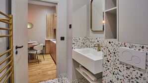 Une salle de bain moderne avec un lavabo blanc, des carreaux de terrazzo et un miroir encadré d’or.