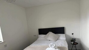 En pænt redt seng med et stribet dynedække og et foldet håndklæde. Der er et lille natbord med en lampe og en plante.