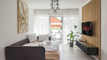 Una moderna camera d'albergo con un letto, un divano, una televisione e un balcone con vista.