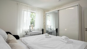 A hotel room with a bed, a bedside table, a mirror, a window with curtains, and a wardrobe.