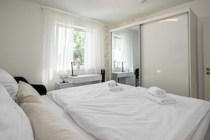 A hotel room with a bed, a bedside table, a mirror, a window with curtains, and a wardrobe.