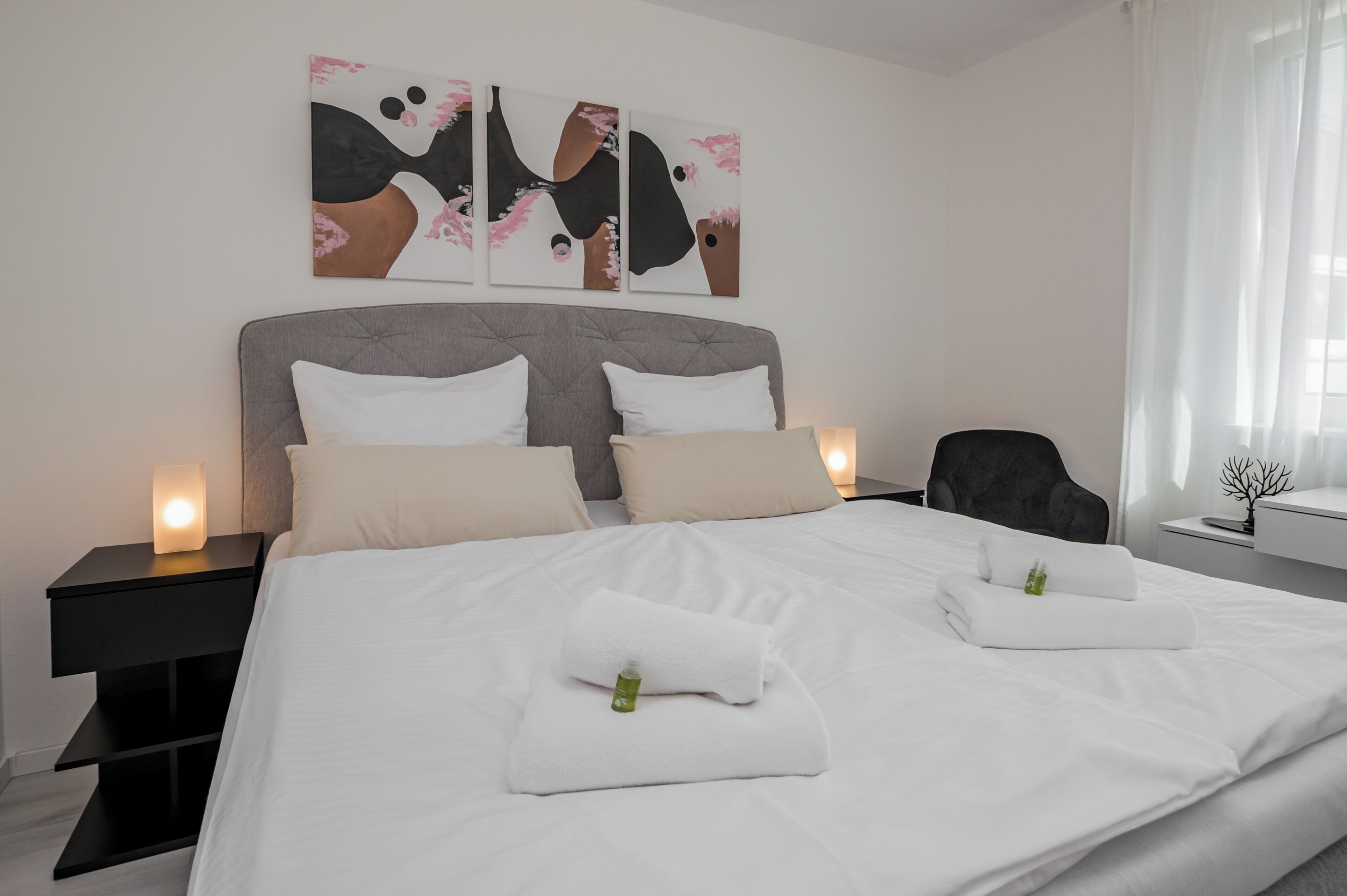 Ein Hotelzimmer mit einem großen Bett, zwei Nachttischen, einem Sessel und einem Kunstwerk an der Wand.