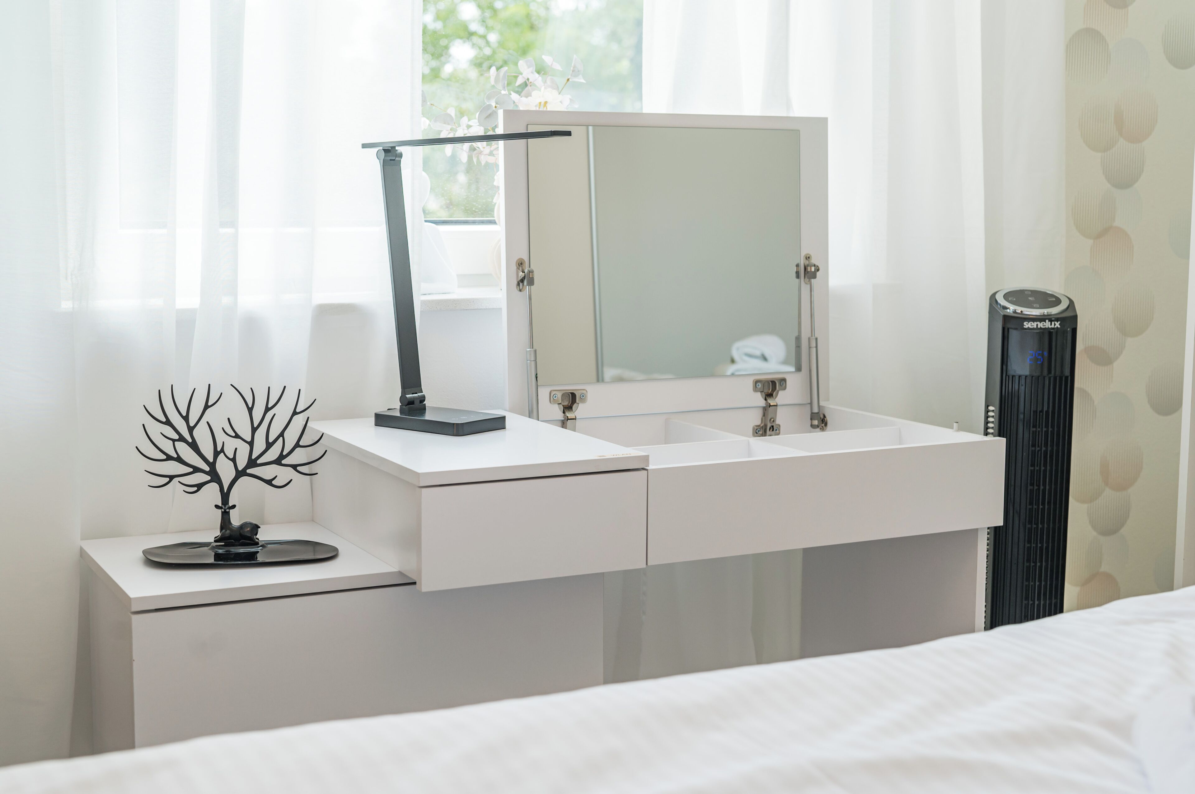 Une chambre d’hôtel avec un lit, une table de chevet dotée d’un miroir, un petit arbre décoratif et un radiateur portatif.