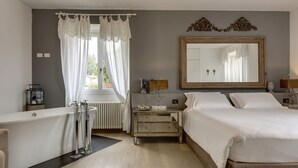 A bedroom with a large bed, a nightstand, a dresser, a mirror, a window with curtains, and a bathtub. - AMORE RENTALS - Villa Barbara with Private Pool and Garden (Palazzuolo sul Senio)