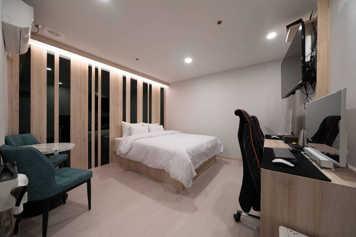 Een moderne hotelkamer met een bed, een bureau met een computer, een stoel en een televisie.
