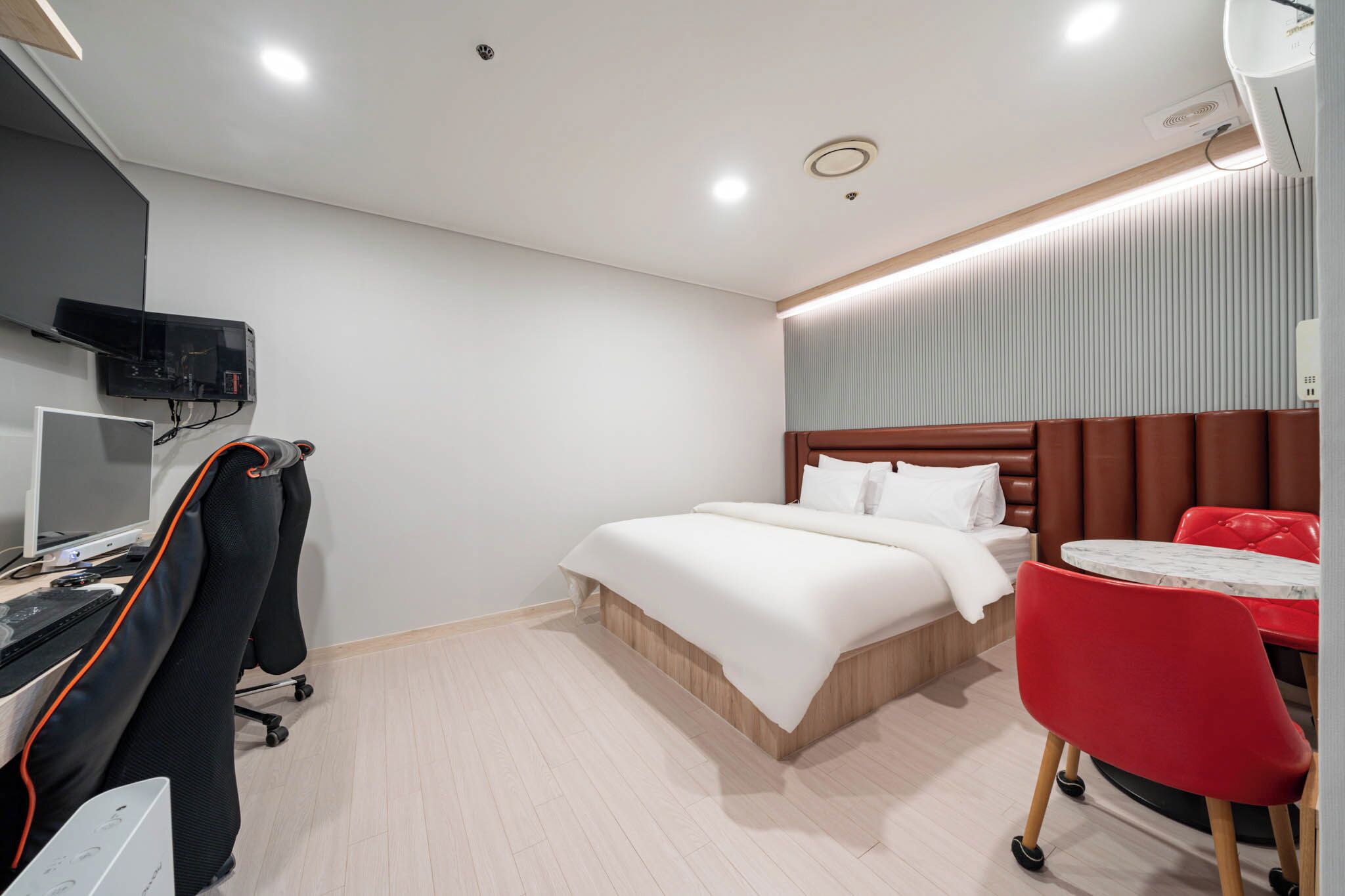 A hotel room with a bed, a desk with a computer, a TV, and a red chair.