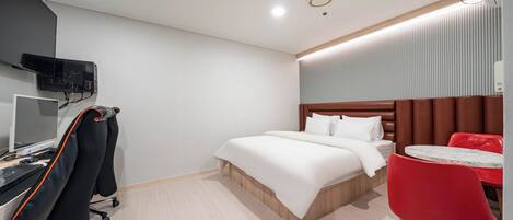 A hotel room with a bed, a desk with a computer, a TV, and a red chair.