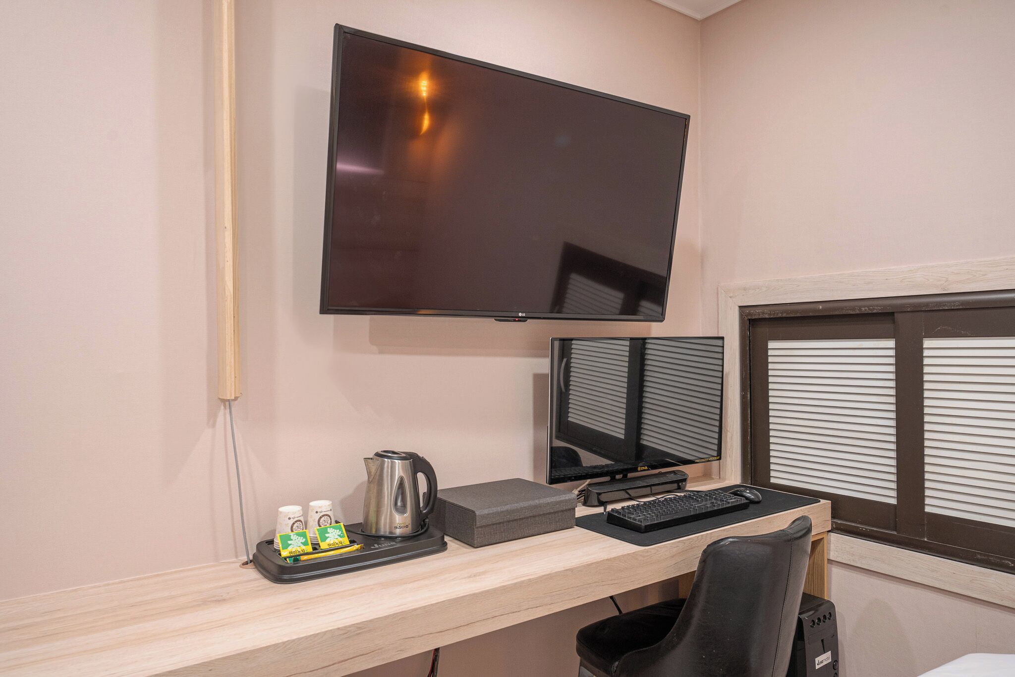 A workspace with a flat-screen TV, two monitors, a keyboard, a coffee maker, and a trash bin.