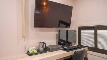 A workspace with a flat-screen TV, two monitors, a keyboard, a coffee maker, and a trash bin.