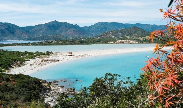 Eine Küstenlandschaft mit Strand, klarem, blauem Wasser und Bergen im Hintergrund.