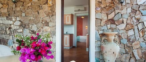 A stone wall entrance leading to a room with a bed, a vase, and a flower arrangement.