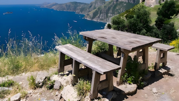 Ein Holztisch mit Bänken auf einer felsigen Anhöhe mit Blick auf die Küste.