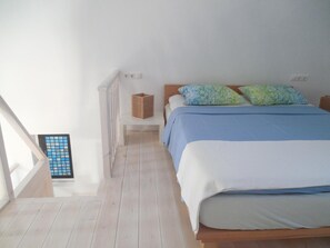 Un dormitorio con cama, almohadas, mesita de noche, ventana y radiador.