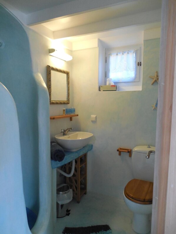 A bathroom with a sink, mirror, toilet, and a window with curtains.