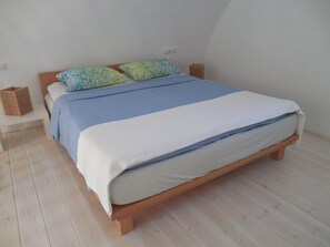 A single bed with a wooden frame, a blue and white bedspread, and patterned pillows. There are two bedside tables with baskets. - Studio 'Avgi' with Sea View, Wi-Fi and Air Conditioning (Kamari)
