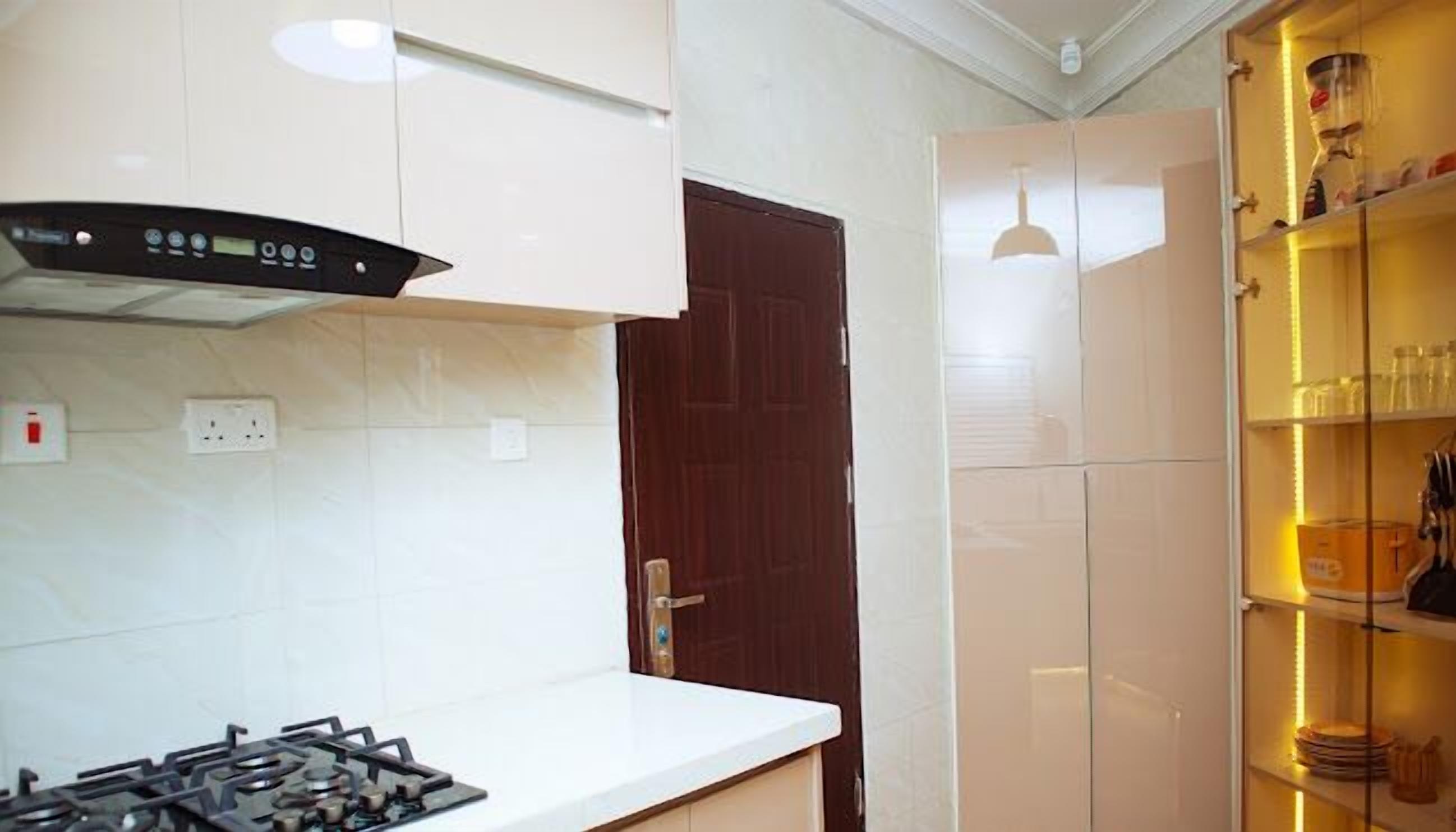 A kitchen with white cabinets, a gas stove, a dark wooden door, and a shelf with glassware.