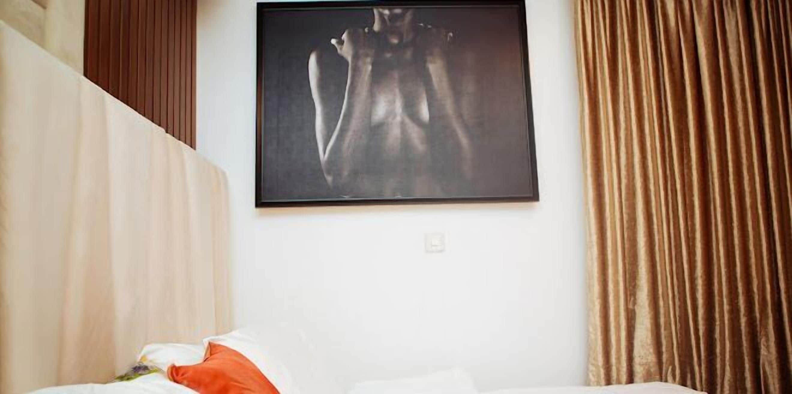 Ein Hotelzimmer mit einem Bett, einem gerahmten Kunstwerk an der Wand und einem Vorhang.