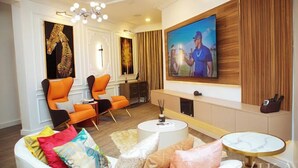 Ein modernes Wohnzimmer mit einem großen Flachbildfernseher, orangefarbenen Sessel, einem weißen Sofa und einem kleinen runden Tisch.