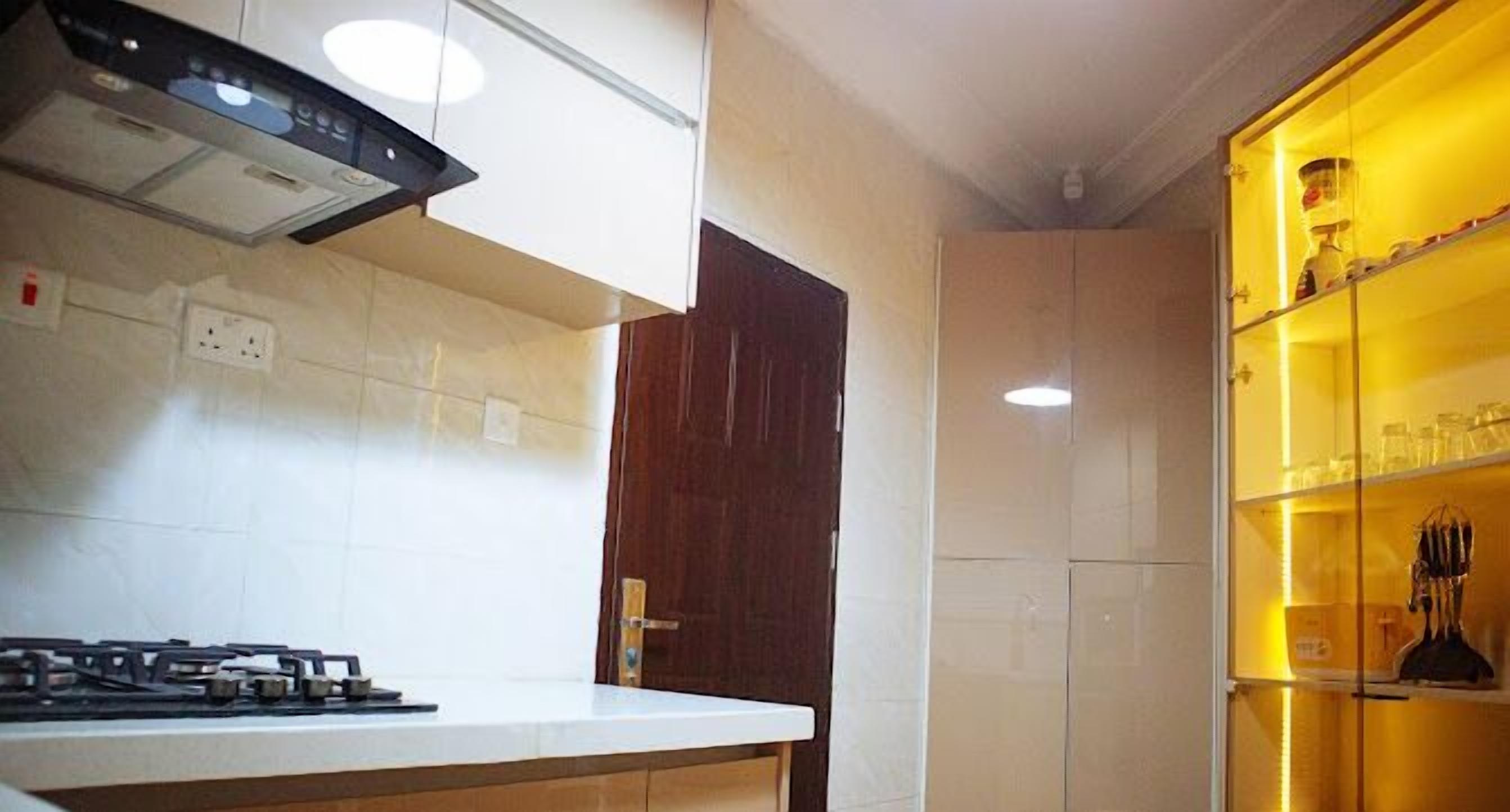 A kitchen with a gas stove, white cabinets, a wooden door, and a yellow-lit cabinet with glassware.