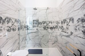 Une salle de bain dotée d’une douche à parois de verre, de murs en marbre et de toilettes avec un tapis.