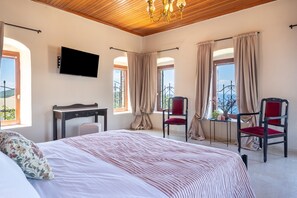 A bedroom with a bed, a desk, two chairs, a TV, and large windows.