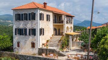 A two-story stone building with a red-tiled roof, a balcony, and a staircase leading to the upper floor.