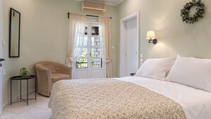 Ein Schlafzimmer mit einem Bett, einem Sessel, einem kleinen Tisch mit Pflanze, einer Tür und einer Wandleuchte.