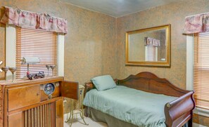 Classic bedroom with a wooden bed, bedside table, and lamp, featuring a window with blinds and a mirror.