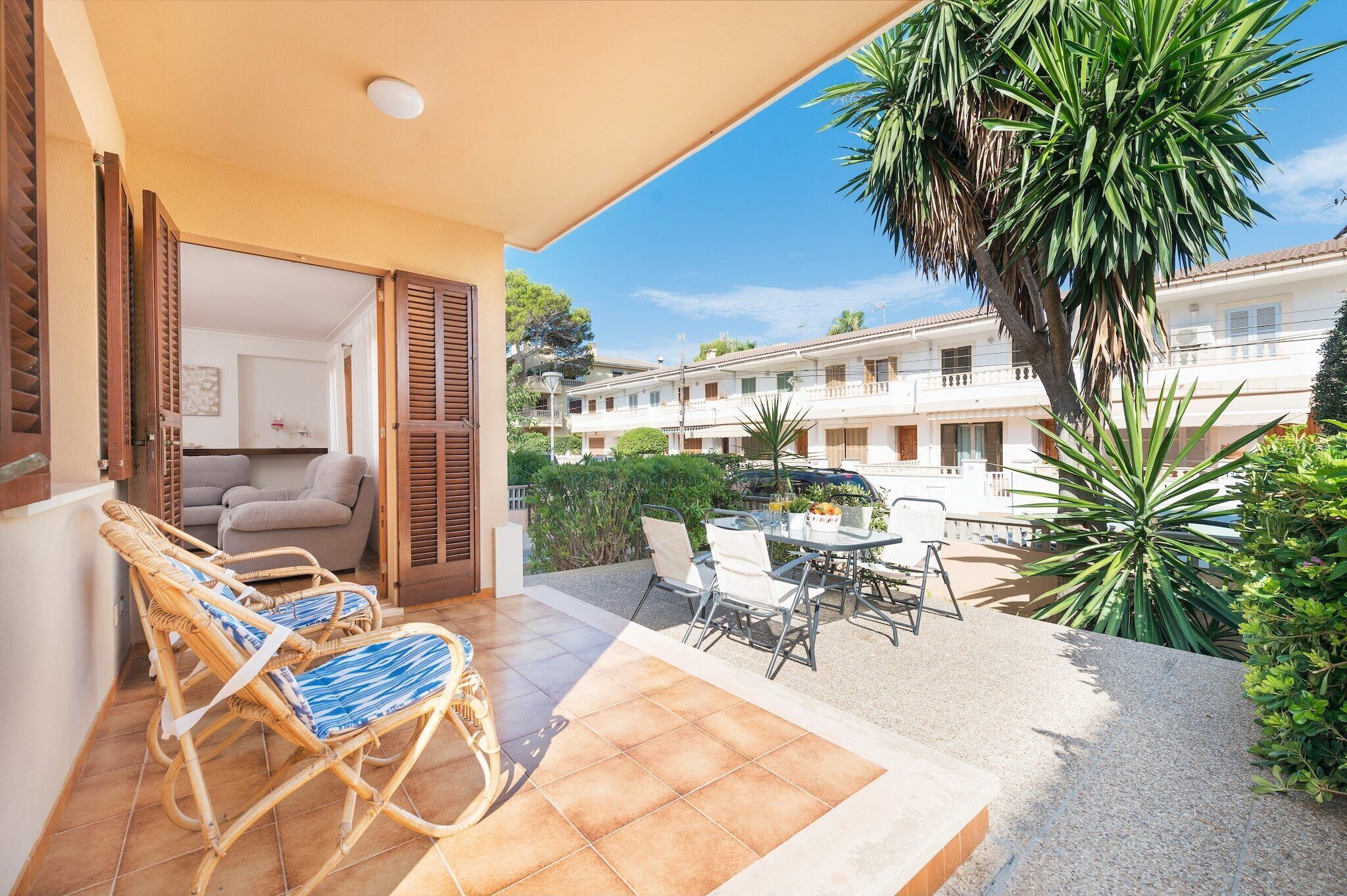 A balcony with wicker chairs and a table, a palm tree, and a view of a residential building.