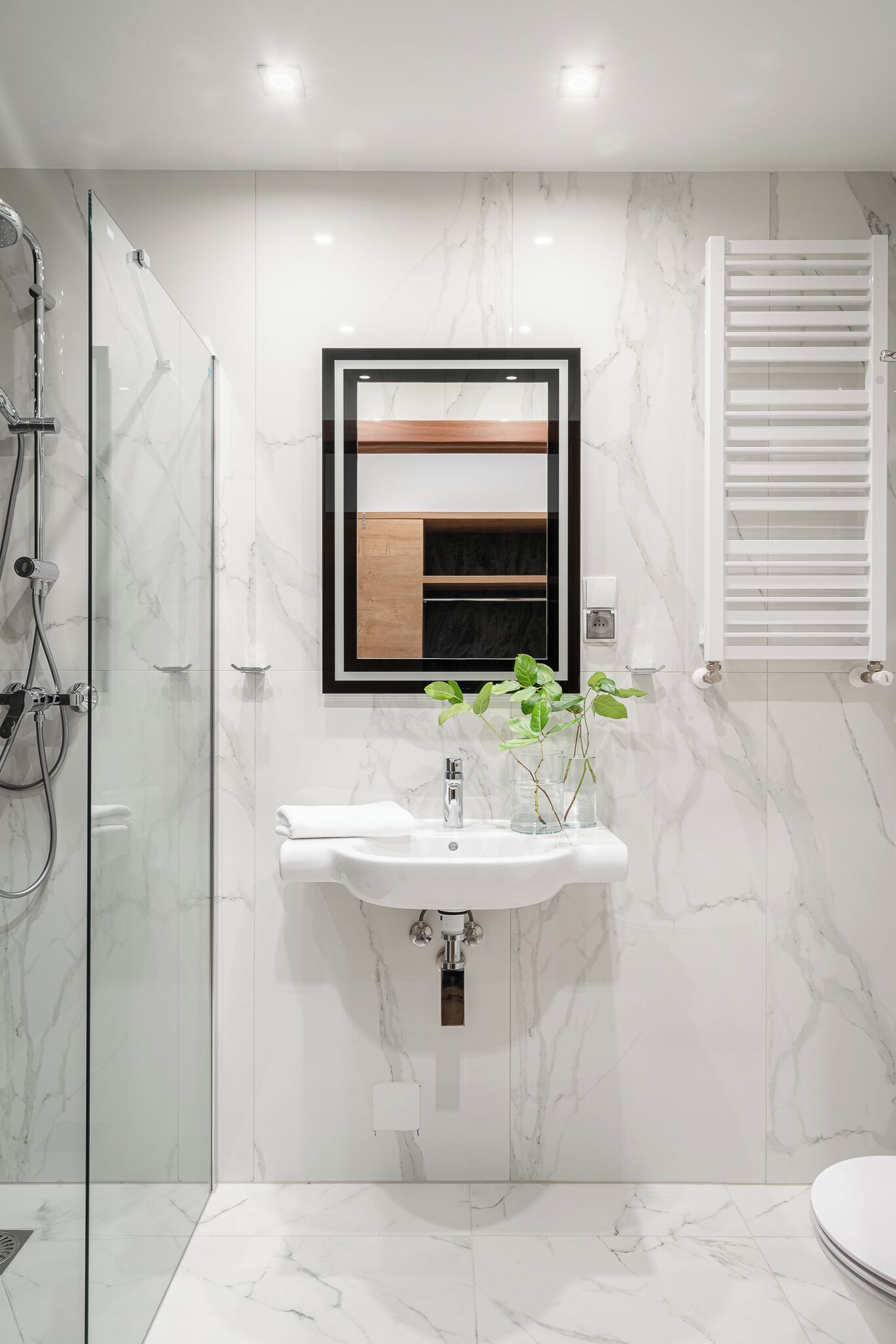 Een moderne badkamer met een douchecabine van glas, een wit wastafelmeubel met een spiegel erboven en een witte handdoek op het aanrecht.