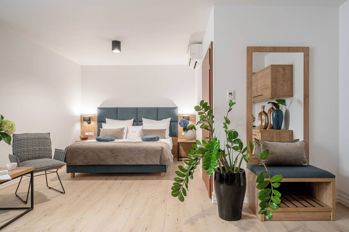 A modern bedroom with a bed, bedside tables, a chair, a bench, and a potted plant.