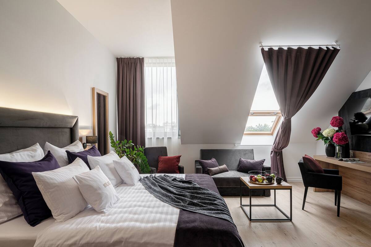A modern hotel room with a large bed, a desk, and a seating area.