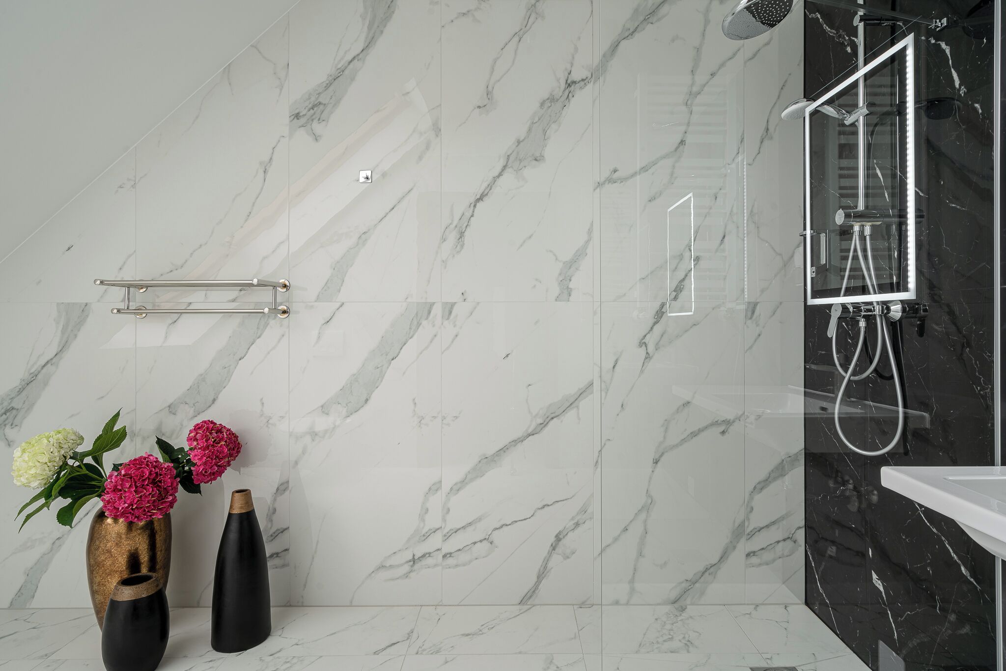 Een moderne badkamer met marmeren wanden, een douche met glazen cabine, en twee vazen met bloemen.