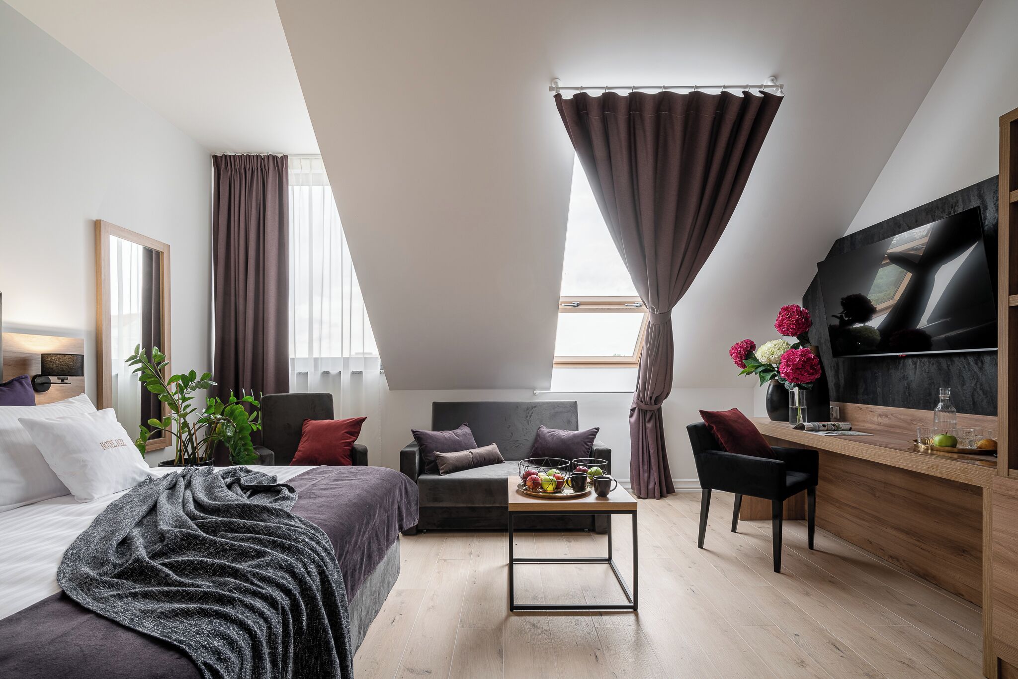 A modern hotel room with a bed, a sofa, a desk, and a TV.