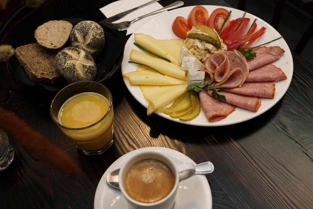 En frukostuppläggning med bröd, ost, skinka, tomater och ett glas apelsinjuice.