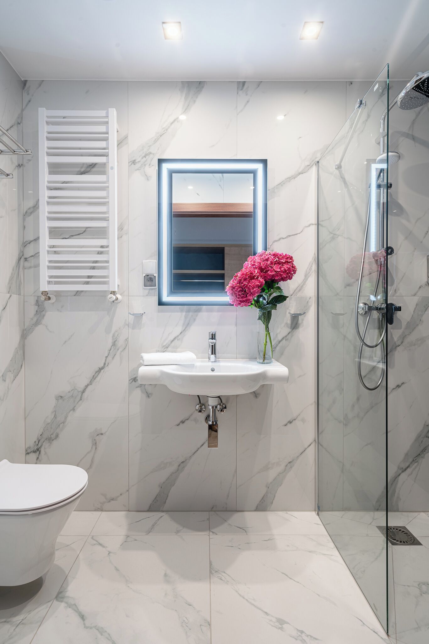 A modern bathroom with a marble floor, a white sink with a mirror, a glass shower enclosure, and a toilet.