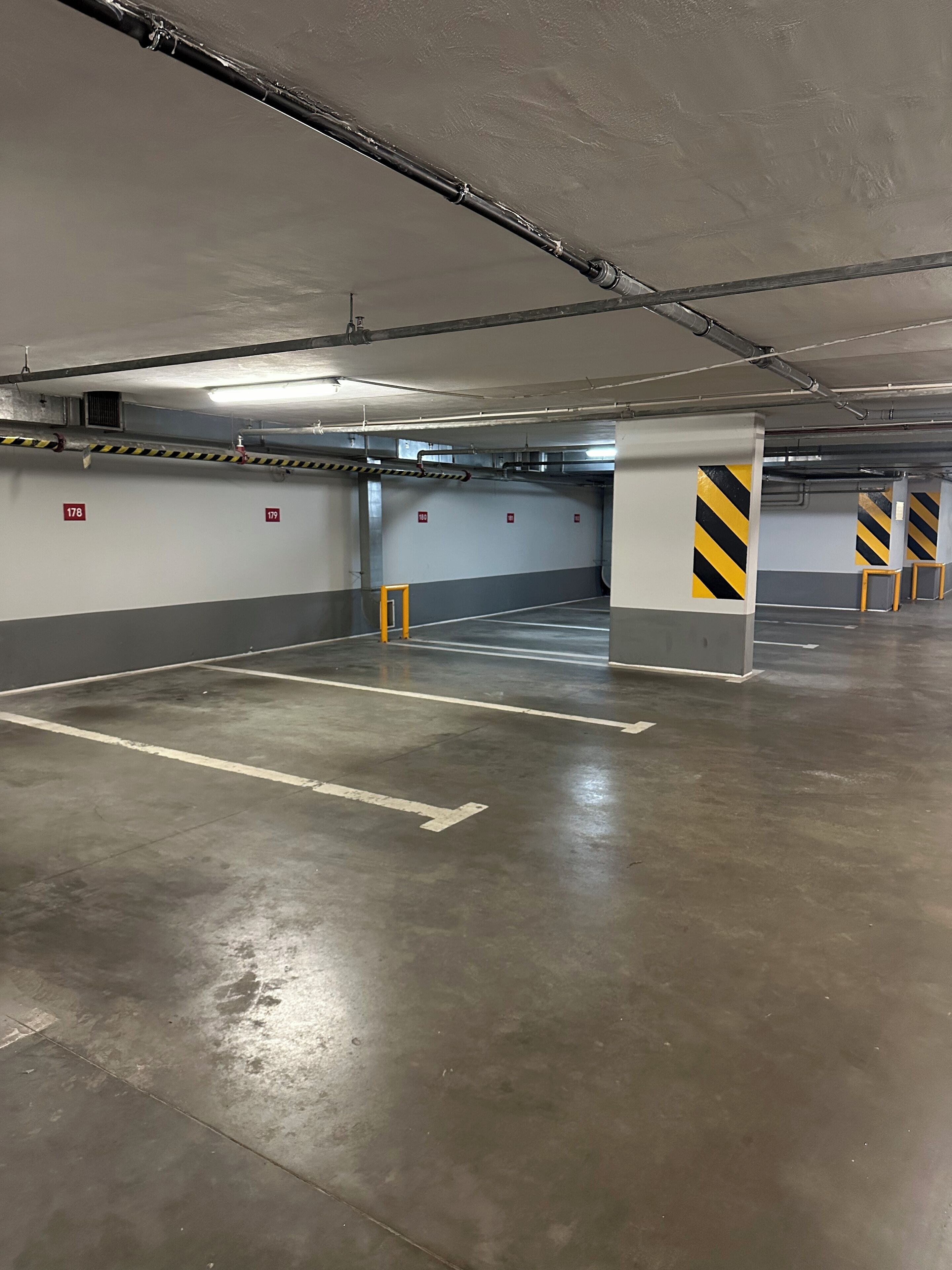 An empty parking garage with concrete floors, marked parking spaces, and yellow and black striped safety barriers.