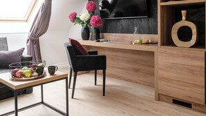 Ein modernes Wohnzimmer mit Fernseher, Holzregalen, einem Esstisch mit Obst und einem großen Fenster mit Vorhängen.